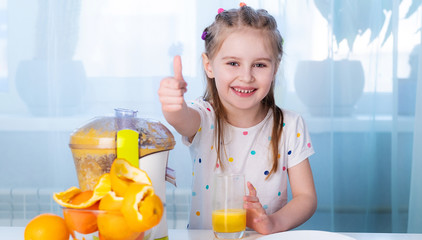 Happy little girl making fresh fruit juice. Smiling with thumbs up