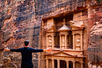 A man is posing in front of the monastery of Petra in the desert in Jordan