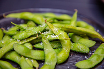 Cooked green Edamame lie on a dark plate in a Japanese restaurant.