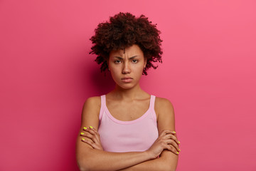 Portrait of dissatisfied insulted dark skinned woman crossed arms over body, looks in displeasure,...