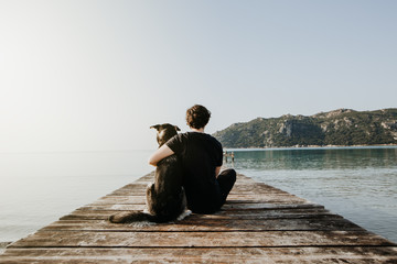 Mensch umarmt Hund auf einem Steg mit Blick auf einen wunderschönen See mit Bergen