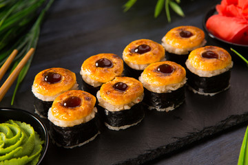 Set of baked sushi rolls with wasabi and ginger on a black background. Japanese oriental cuisine