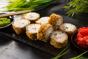 Set of baked sushi rolls with wasabi and ginger on a black background. Japanese oriental cuisine