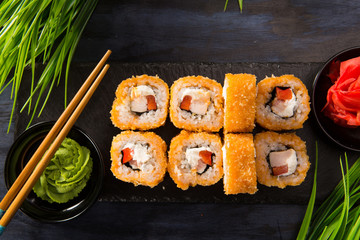Set of baked sushi rolls with wasabi and ginger on a black background. Japanese oriental cuisine