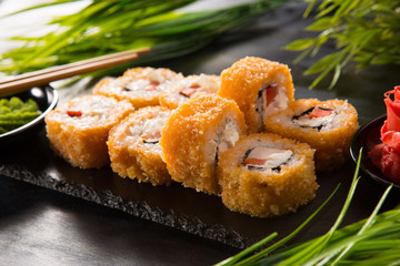 Set of baked sushi rolls with wasabi and ginger on a black background. Japanese oriental cuisine