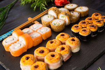 Set of baked sushi rolls with wasabi and ginger on a black background. Japanese oriental cuisine