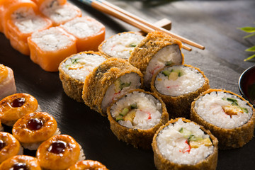 Set of baked sushi rolls with wasabi and ginger on a black background. Japanese oriental cuisine