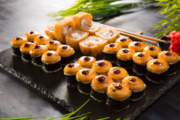 Set of baked sushi rolls with wasabi and ginger on a black background. Japanese oriental cuisine
