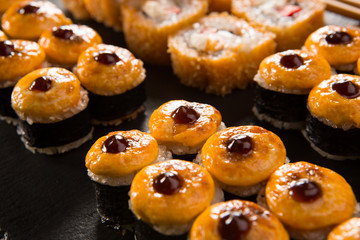 Set of baked sushi rolls with wasabi and ginger on a black background. Japanese oriental cuisine