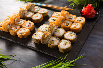 Set of baked sushi rolls with wasabi and ginger on a black background. Japanese oriental cuisine