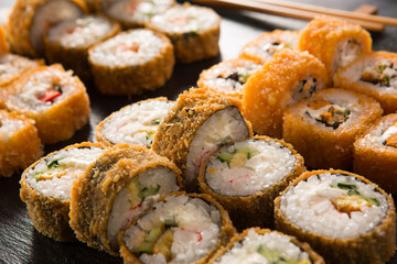 Set of baked sushi rolls with wasabi and ginger on a black background. Japanese oriental cuisine