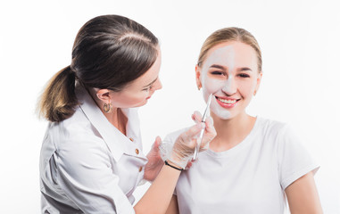 Beautician applies a mask on the face of a young beautiful girl, on a white background
