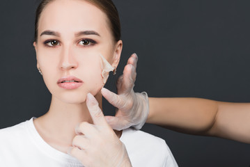 Beautician removes the mask from the face of a young beautiful girl, on a gray background, the concept of rejuvenation and youth