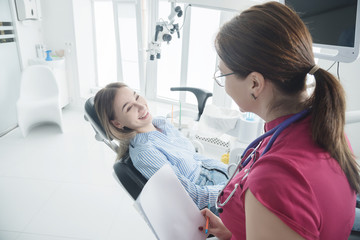 The dentist consults a patient sitting in a chair in the dental office