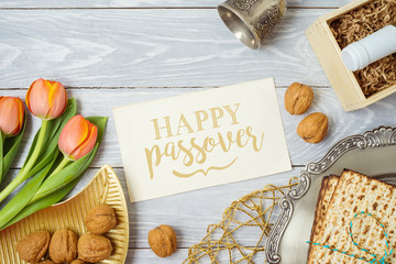 Jewish holiday Passover greeting card with matzo, seder plate, wine and tulip flowers on wooden table.