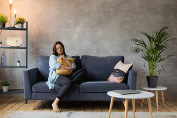 Obraz premium Worried woman sitting on couch at home. Frustrated confused female feels unhappy, problems in personal life, quarrel break up with boyfriend and unexpected pregnancy concept