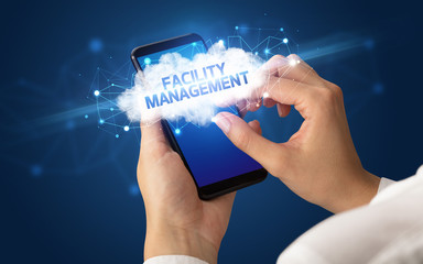 Female hand touching smartphone with FACILITY MANAGEMENT inscription, cloud business concept