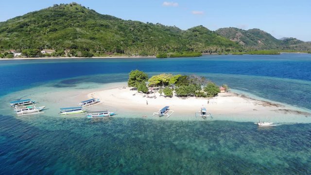 Fly over a little beautiful island at the shoreline of Lombok, Indonesia. Aerial view over beautiful sandy beaches and blue turquoise water. Small tourist boats anchor on the beach. holiday feeling
