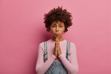 Please I beg you. Sorrowful dark skinned ethnic woman holds hands in pray, asks for apology or...