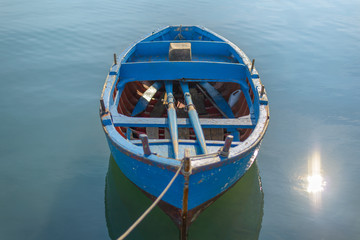 Obraz premium Blue Boat in lake. Sunshine on blue water. Wooden blue boat on calm water tied to the harbor by a rope. 