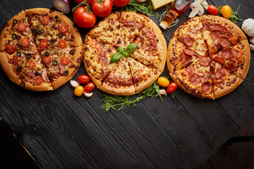 Freshly served, three various pizzas placed among tasty ingredients. Top view