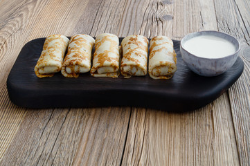 wheat crepes with filling and sour cream on black wooden tray and wooden background