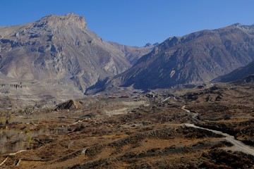 Desert scenery of Mustang Land around Muktinath, Nepal. Winding road towards buildings. During trekking around Annapurna, Himalayas.
