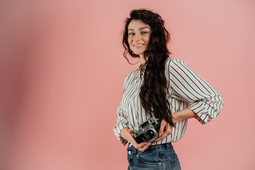 Cheerful young girl photographer posing with a camera on a pink background