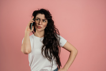 Fototapeta premium The girl speaks on the phone, portrait on a pink background