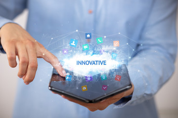 Businessman holding a foldable smartphone with INNOVATIVE inscription, technology concept