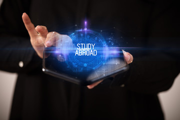 Young man holding a foldable smartphone with STUDY ABROAD inscription, educational concept