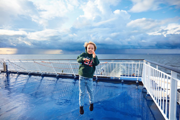 smiling kid having fun on the upper deck of cruise ship after heavy rain storm on the sea during...