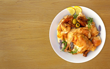The concept of simple healthy food. White dish with grilled chicken slices with crust with sprigs of herbs, lemon wedges and olives on wooden background with copy space. Delicious cooked chicken