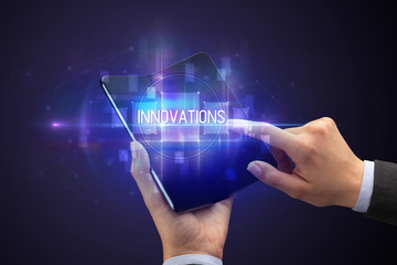 Naklejka premium Businessman holding a foldable smartphone with INNOVATIONS inscription, new technology concept