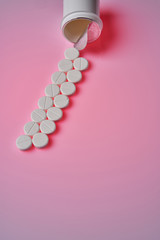 White round tablets scattered near plastic bottle of pills on pink background
