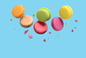 Colorful macaroons or macarons falling or flying over blue background. Copy space.