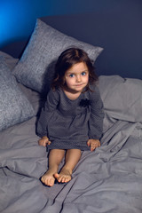 girl in a gray dress sits on a bed with pillows in a bedroom