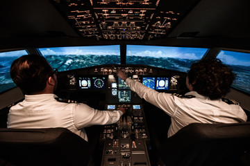 Two pilots during the flight. They are changing commands in the cockpit.  The plane is about to fly over the mountains