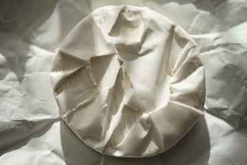 Whole round camembert cheese on a sunny wrapping paper. Top view.