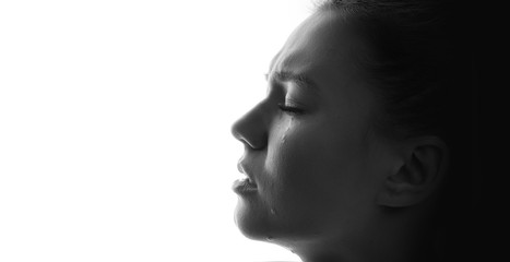 Black and white portrait of beautiful young sad woman crying with closed eyes. White background....