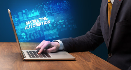 Businessman working on laptop with MARKETING AUTOMATION inscription, cyber technology concept