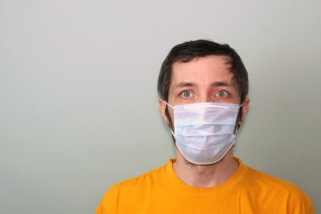 Middle-aged adult man in a yellow T-shirt on a gray background in a medical mask. Disease protection coronavirus epidemic problem from China