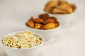 Coconut flakes and almonds in three white bowls on a white surface