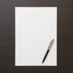 Template of white paper with pen on dark wenge color wooden background.