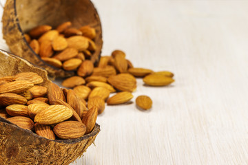 Two half coconut shell with almonds on a white background