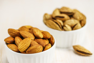 Two white bowls with peeled and unpeeled almonds on a white surface