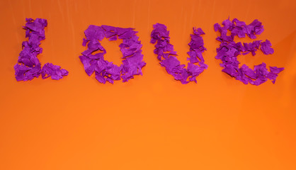 The word love on an orange background. Love from pieces of pink paper.