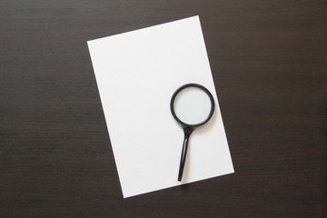 Template of white paper with magnify on dark wenge color wooden background.