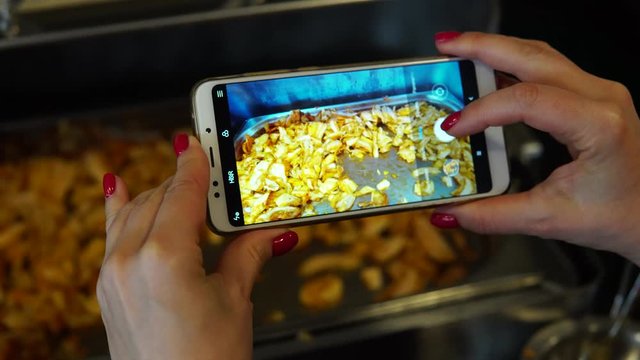 A woman photographs on a smartphone roasted meat in a restaurant buffet. Social network blogger concept photo. Healthy and tasty food.