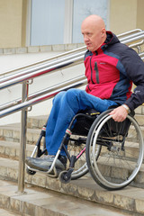 Fototapeta na wymiar Minsk, Belarus, February 29,2020 - a man in a wheelchair independently descends a steep staircase with steel railings, active rehabilitation of disabled people, barrier-free 